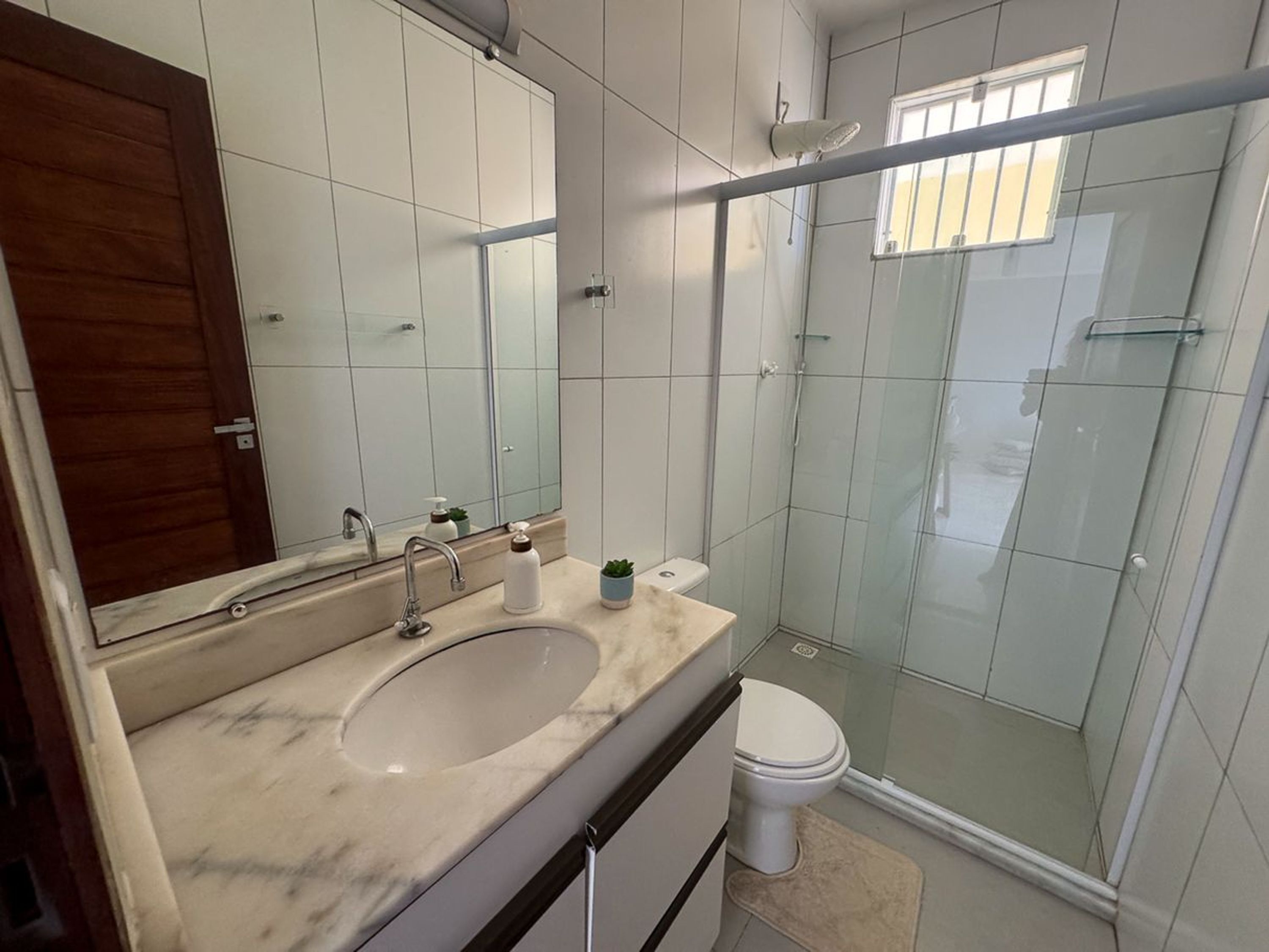 Un baño con lavamanos de mármol, inodoro, cabina de ducha con mampara de vidrio y un espejo grande.