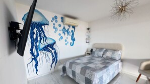 A bedroom with a large wall mural of a jellyfish, a bed with a patterned blanket, a nightstand, a chair, and a ceiling light fixture. - Casa com rea Gourmet Piscina e Vista do Mar (Canguaretama)
