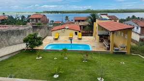 A residential area with a swimming pool, two yellow sun loungers, and a view of the sea. - Casa com rea Gourmet Piscina e Vista do Mar (Canguaretama)