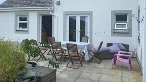 Een wit huis met een patio, inclusief een tafel met stoelen, een bank en een kleine tuin met planten.