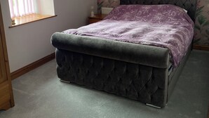 Een slaapkamer met een bed met een gebostelde hoofdbord, bloemenbehang, een raam met zonwering en een radiator.