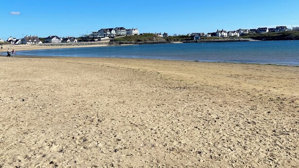 Een strand met een heldere lucht, zandstrand en huizen op de achtergrond.
