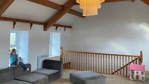 Een ruime loft met zichtbare houten balken, een grote kroonluchter en een gezellige zithoek met een trap en een poppenhuis.