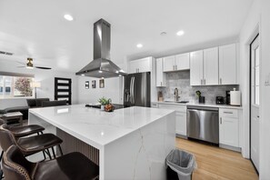A modern kitchen with white cabinets, stainless steel appliances, a marble island, and a ceiling fan. - Beautiful 3-bedroom house in peaceful Scottsdale perfect for relaxing stays (Scottsdale)