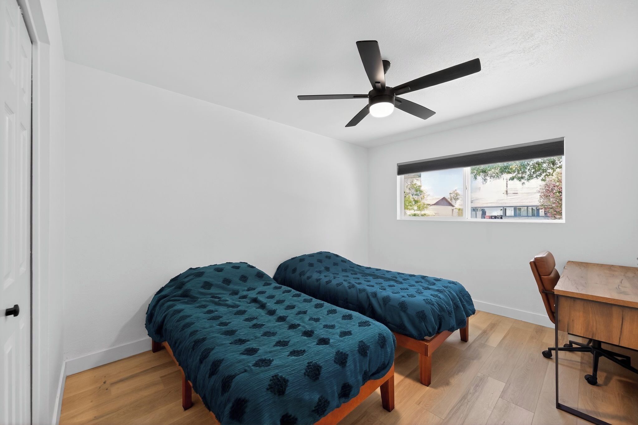 Une chambre avec deux lits simples, un ventilateur de plafond, une fenêtre avec vue et un bureau en bois.
