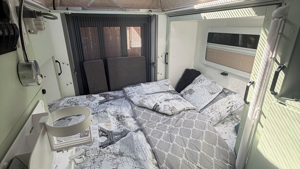 En kompakt autocamper indretning med seng, lille tekøkken, vindue og loftventilator.