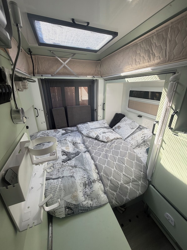 Ein kompaktes Wohnmobil-Interieur mit Bett, kleiner Küchenzeile, Fenster und Deckenventilator.