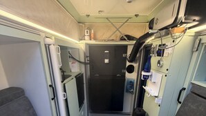 En smal korridor med et ternet gulv, et lille bord med en computer, og en dør for enden.