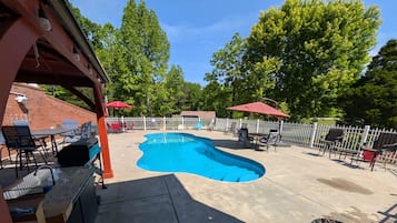 A backyard with a swimming pool, outdoor furniture, and a covered patio area.