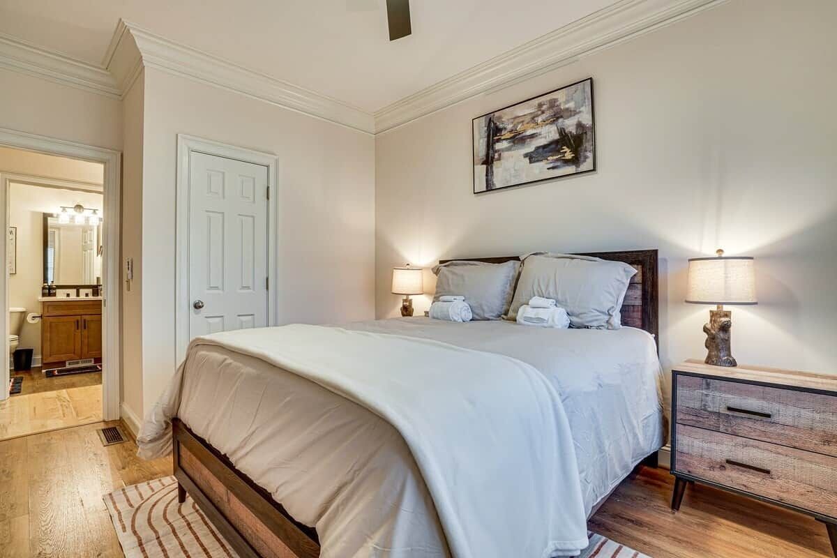 A bedroom with a bed, bedside lamps, a nightstand, a door, and a painting on the wall.