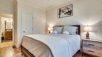 A bedroom with a bed, bedside lamps, a nightstand, a door, and a painting on the wall.