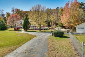 A residential driveway leading to a house with a fenced yard and autumn-colored trees.