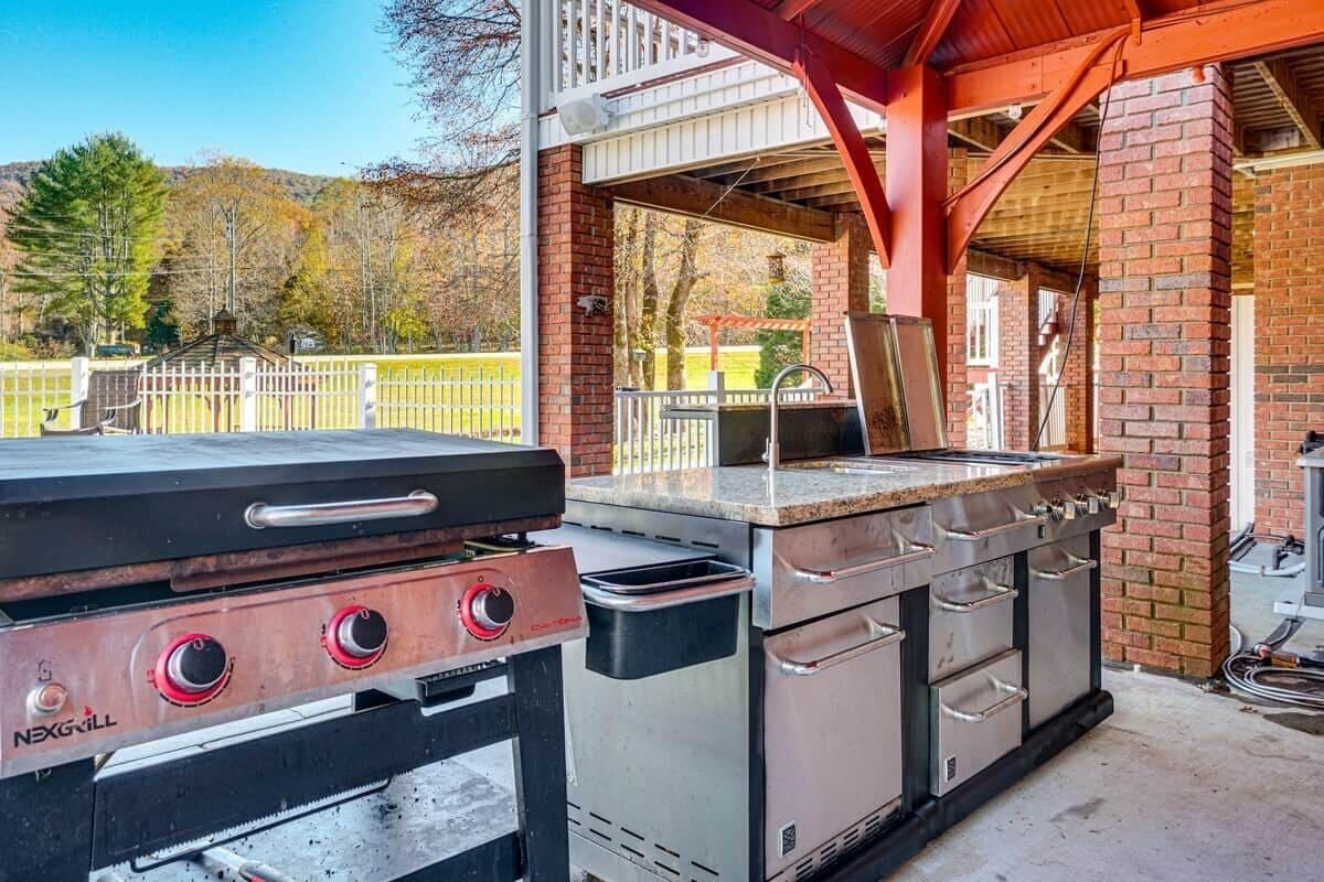 Une cuisine extérieure équipée d’un barbecue, d’un évier et d’un four encastré.