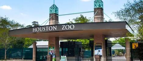 The entrance to Houston Zoo with a sign, two towers, and a gate.