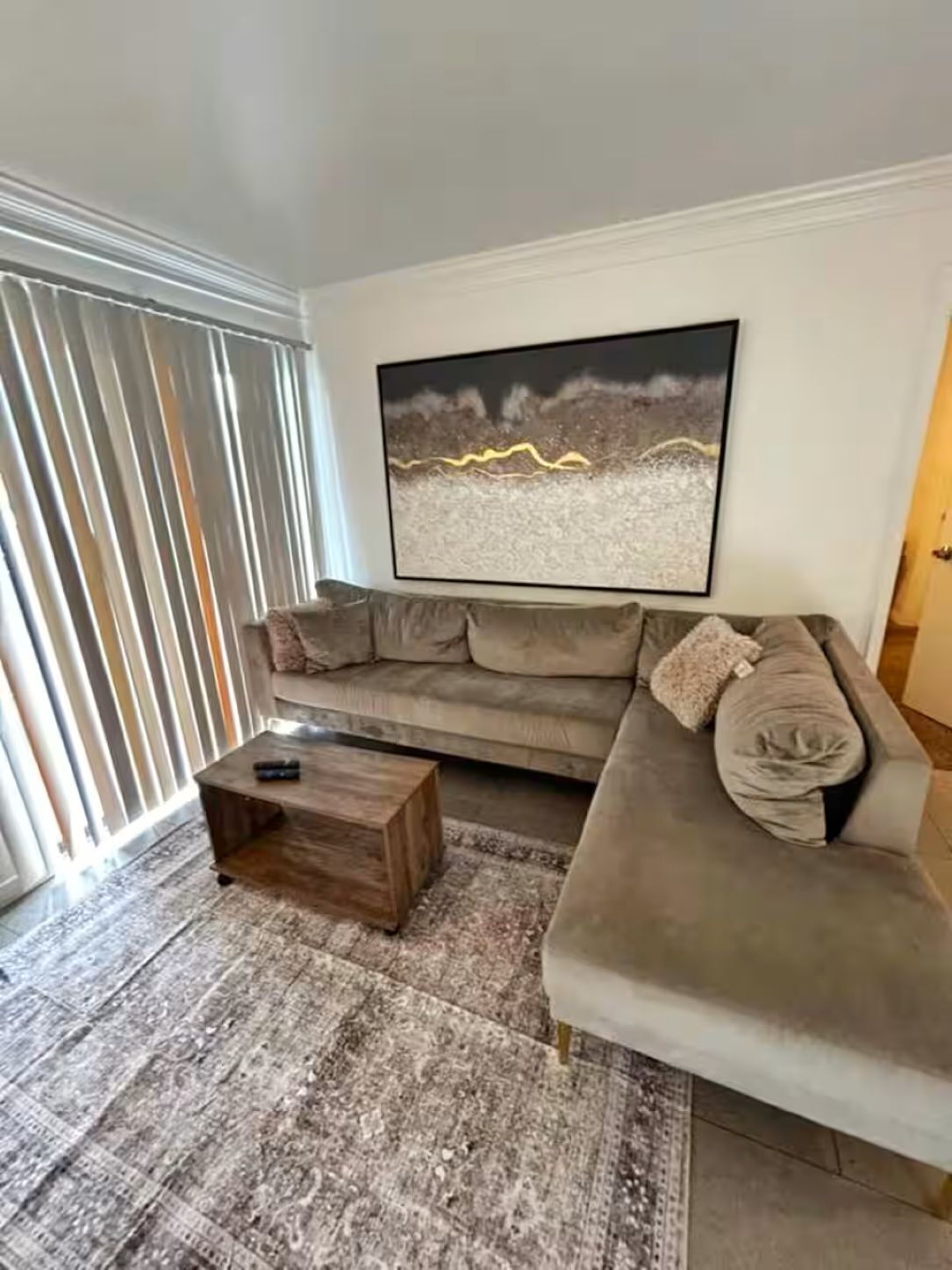 A living room with a sectional sofa, a coffee table, and a large abstract painting on the wall.