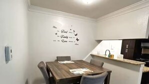 A dining area with a wooden table and chairs, a kitchen in the background, and a wall decal with text and butterflies. - Pleasant King 1Bed 1Bath Near Med Center with Pool (Houston)