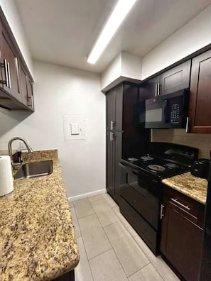 Una cocina con encimeras de granito, estufa, microondas y armarios de madera oscura.