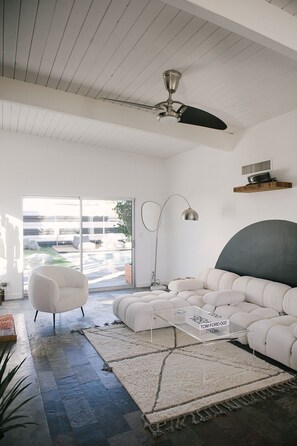 A modern living room with a white sofa, a coffee table, a floor lamp, and a ceiling fan. - Electric Lady House Palm Springs Alexander (Palm Springs)