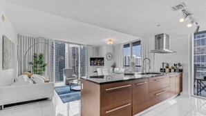 A modern kitchen with a central island, large windows, and a view of high-rise buildings. - The Club at Brickell Bay (Miami)