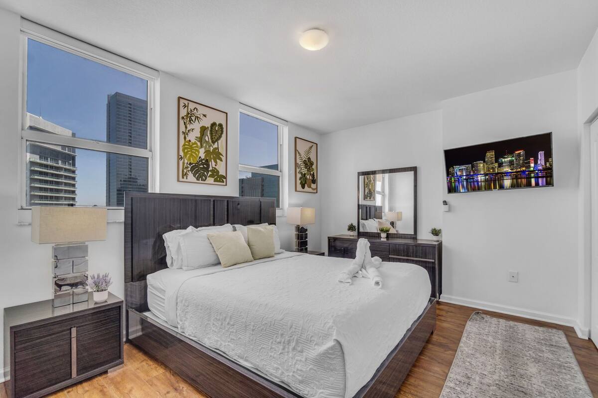 Habitación de hotel moderna con una cama grande, vistas a la ciudad, un escritorio con lámpara y obras de arte en las paredes.