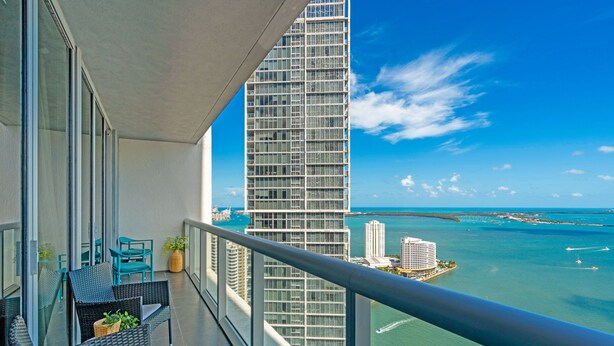 A balcony with wicker furniture, a view of a tall building, and a body of water. - The Club at Brickell Bay (Miami)