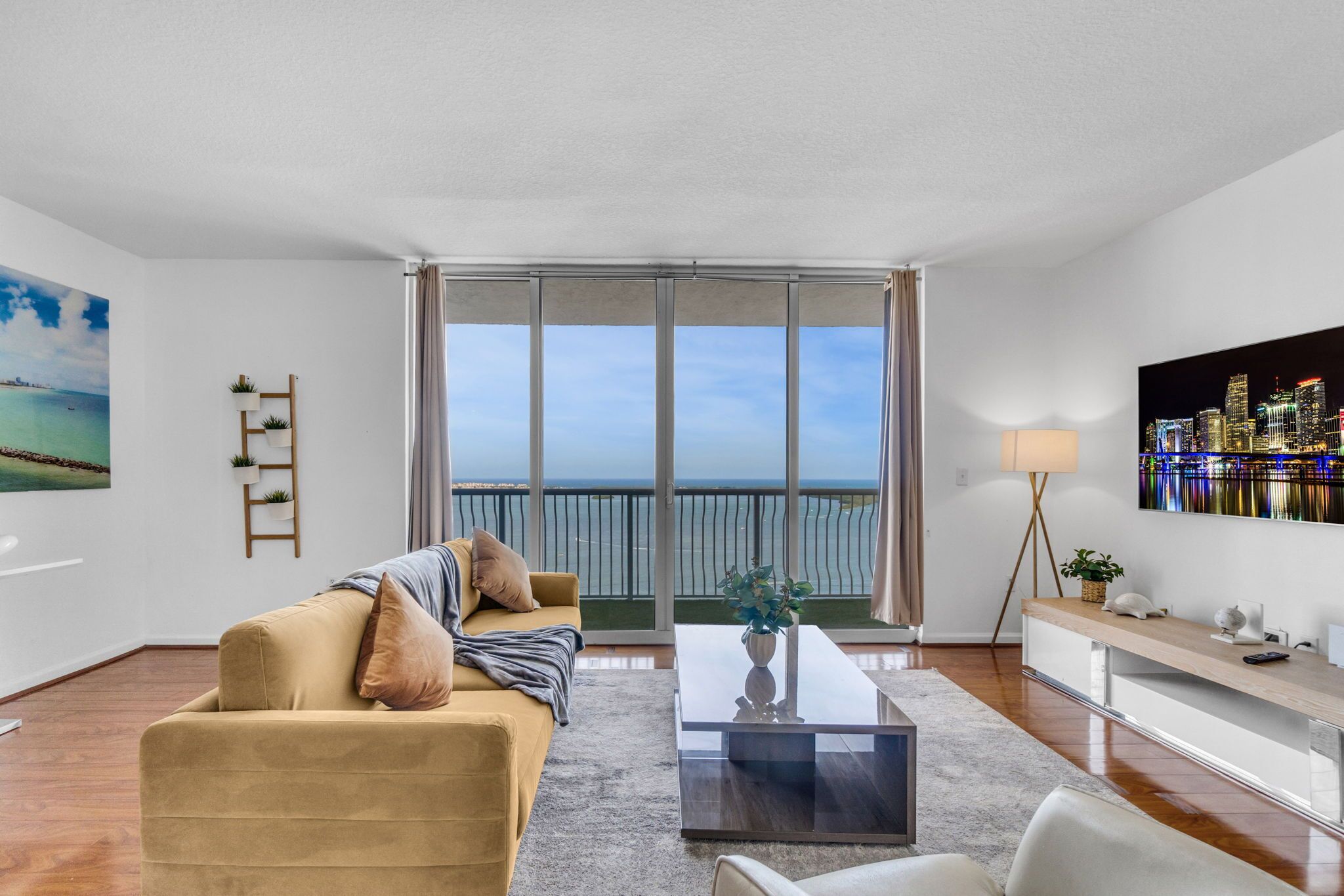 A modern living room with a sofa, a coffee table, a TV, and a balcony with a view.
