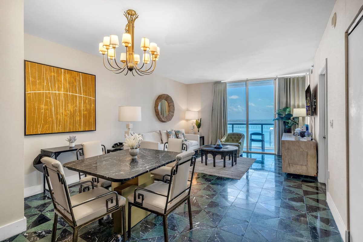 A dining area with a marble table, chairs, a chandelier, and a large abstract painting.