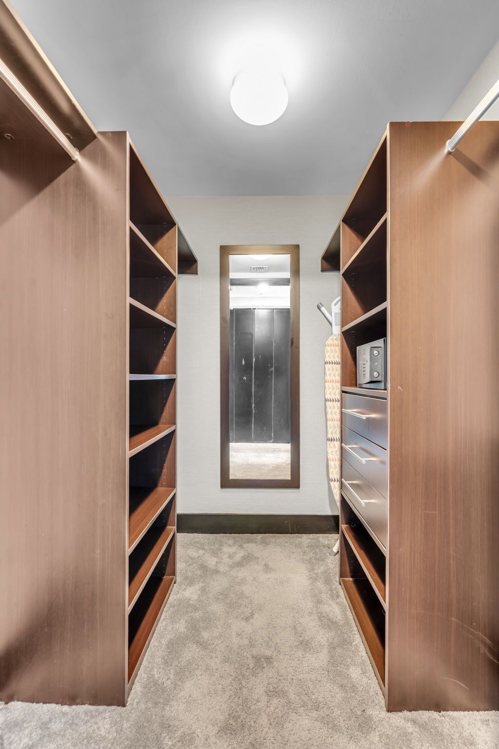 A walk-in closet with built-in shelving, a window, and a ceiling light.