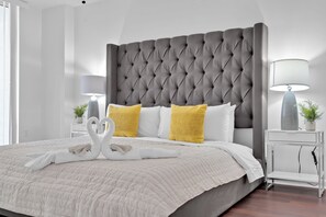 A neatly made bed with a tufted headboard, white and yellow pillows, and a swan-shaped towel arrangement. - The Club at Brickell Bay (Miami)