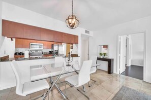 A modern kitchen with a glass dining table, white chairs, and a hanging light fixture. - The Club at Brickell Bay (Miami)