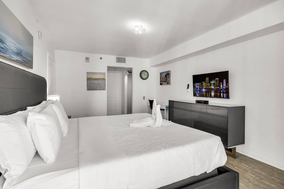 Una habitación de hotel moderna con una cama grande, un televisor, un aparador y un cuadro en la pared.