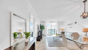 A modern hotel room with a large mirror, a sofa, a dining table, and a view of the city. - The Club at Brickell Bay (Miami)
