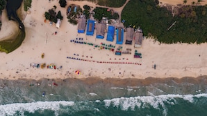 Luchtbeeld van een strand met een rij gebouwen met blauwe daken, een zandstrand en de oceaan.