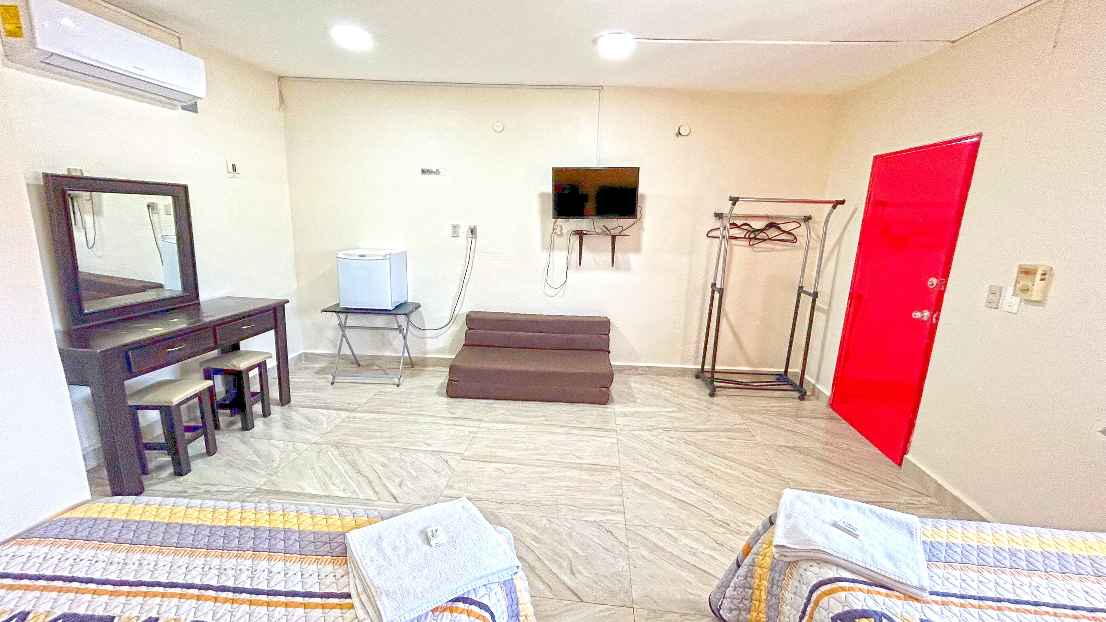 Camera d'albergo con un letto, una scrivania con una sedia, una TV, un tavolino, una porta rossa e una TV a muro.