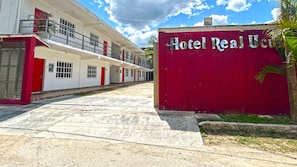 Un bâtiment à la façade rouge et blanche, une enseigne indiquant « Hôtel Real Uco », et une entrée pavée.
