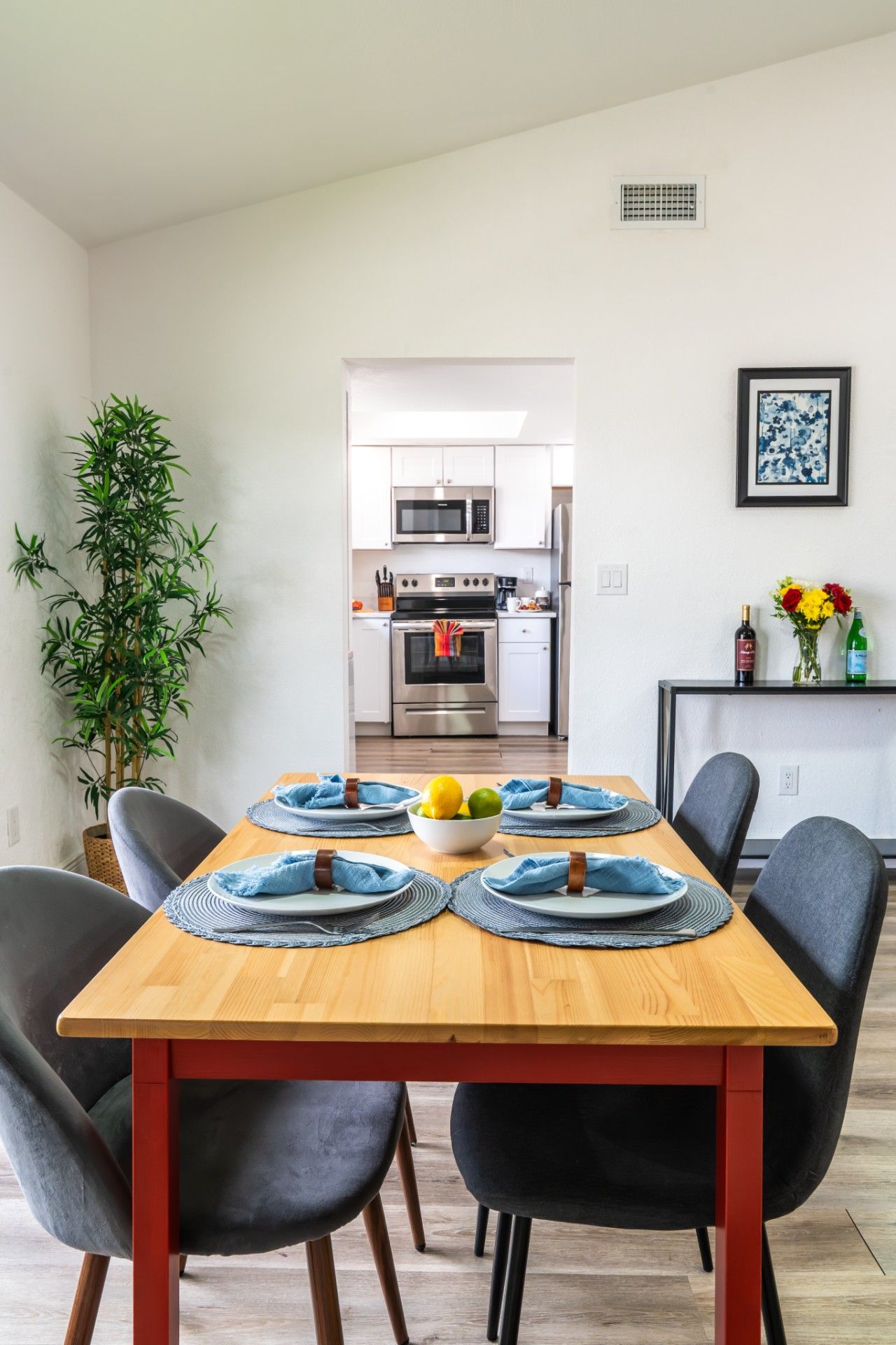 A dining area with a wooden table set for four, chairs, and a kitchen in the background.