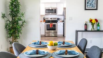 A dining area with a wooden table set for four, chairs, and a kitchen in the background.