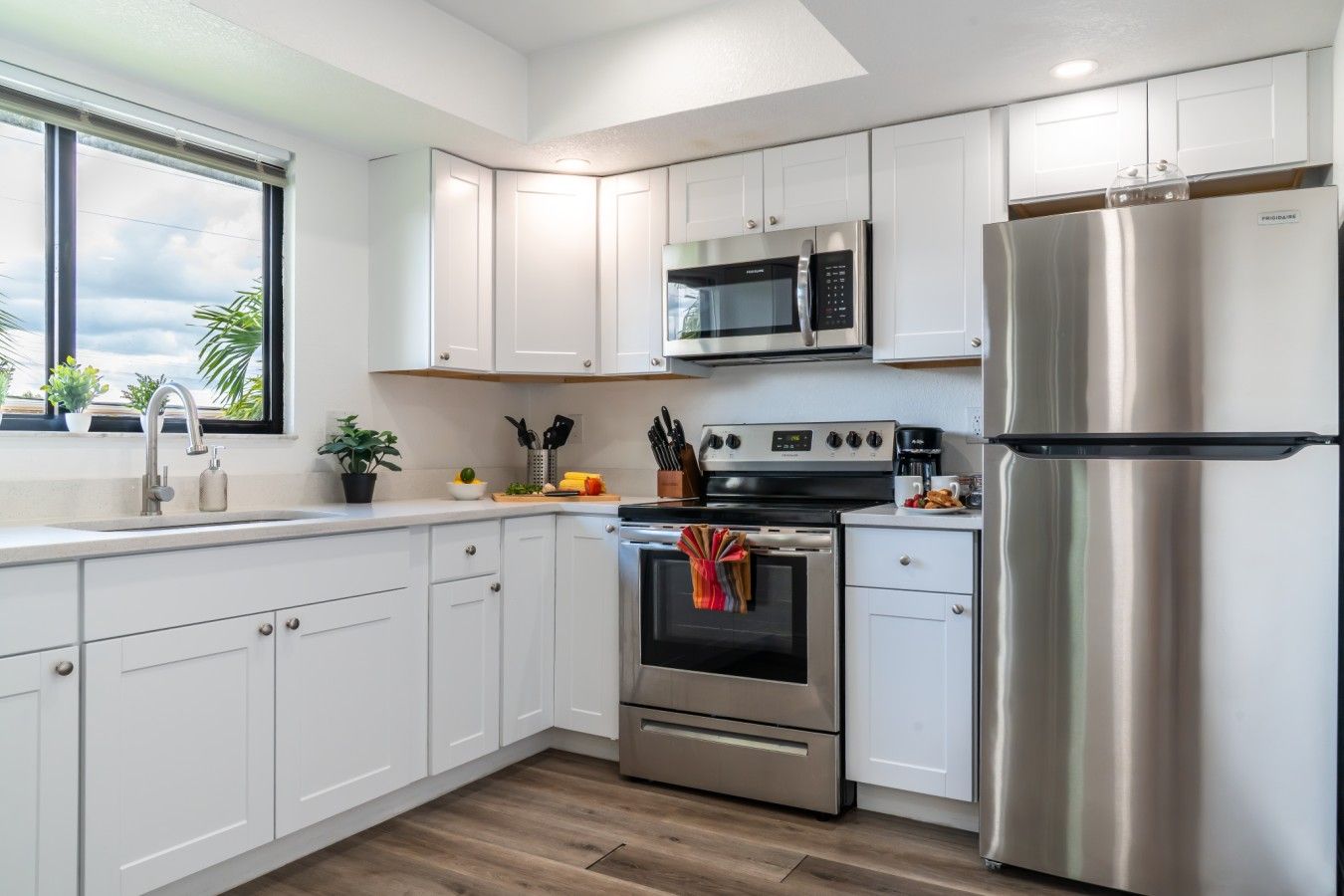 A modern kitchen with white cabinets, stainless steel appliances, and a window with a view.