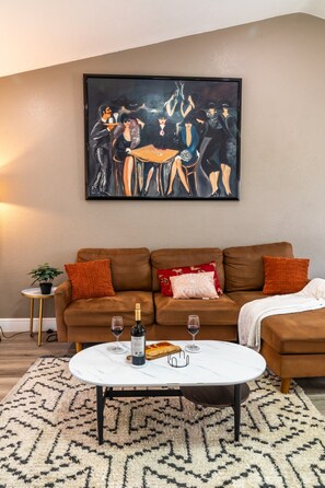 A living room with a brown sofa, a white coffee table, and a painting on the wall. - Central Coral Gem: BBQ Patio | Minutes to River (Cape Coral)