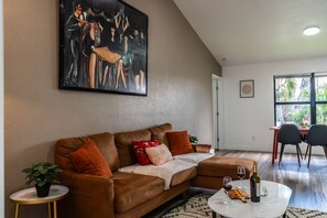 A living room with a brown leather sofa, a coffee table with wine glasses, and a painting on the wall. - Central Coral Gem: BBQ Patio | Minutes to River (Cape Coral)