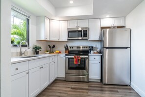A modern kitchen with white cabinets, stainless steel appliances, and a wooden floor. - Central Coral Gem: BBQ Patio | Minutes to River (Cape Coral)