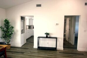 Un salón amplio con mesa de comedor, una planta en maceta y una cocina al fondo.