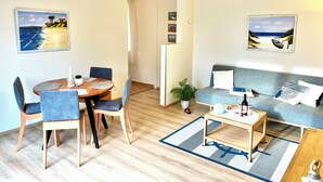 A modern living room with a round wooden table, blue chairs, a grey sofa, and two beach-themed paintings on the walls. - Baltic Sea time-out - near Darß - relaxation in the midst of nature (Pruchten)