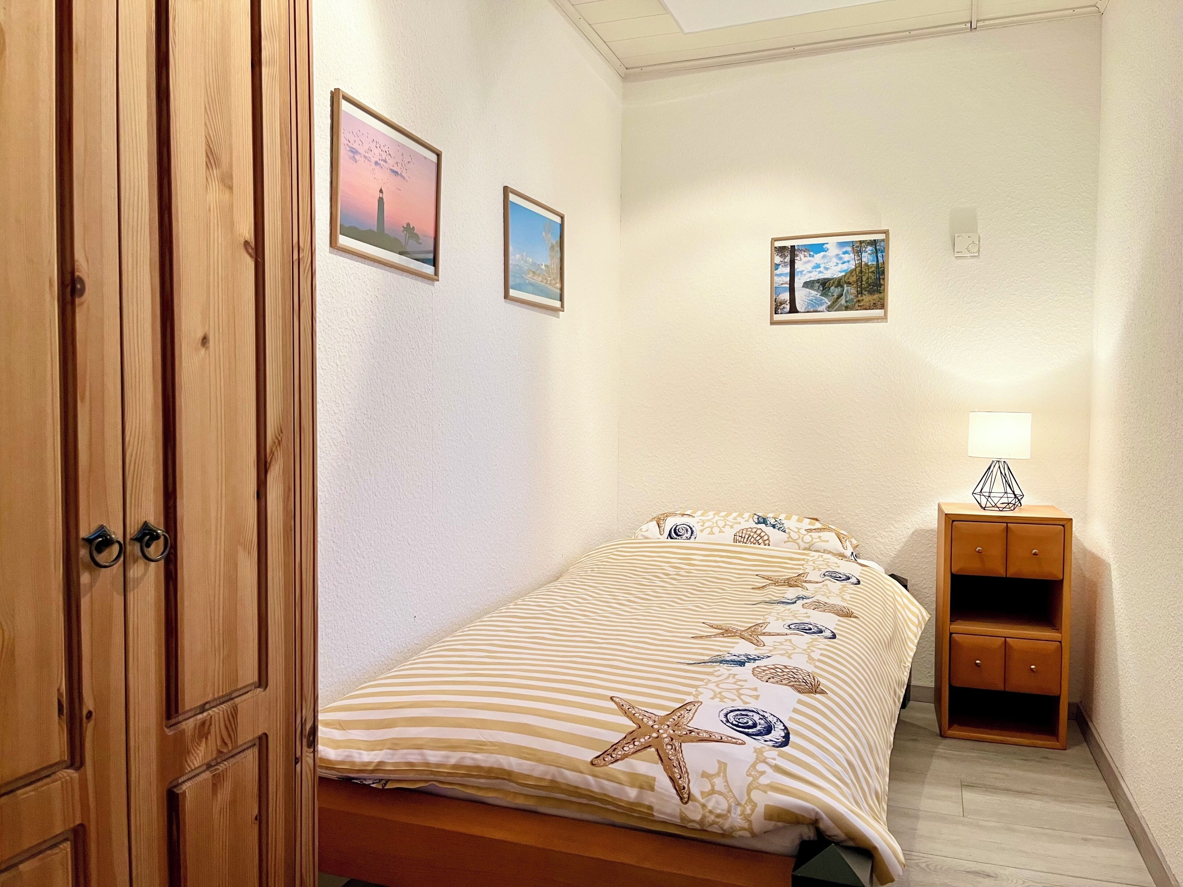 Ein Schlafzimmer mit einem Bett, einem Nachttisch, einer Lampe und zwei gerahmten Bildern an der Wand.