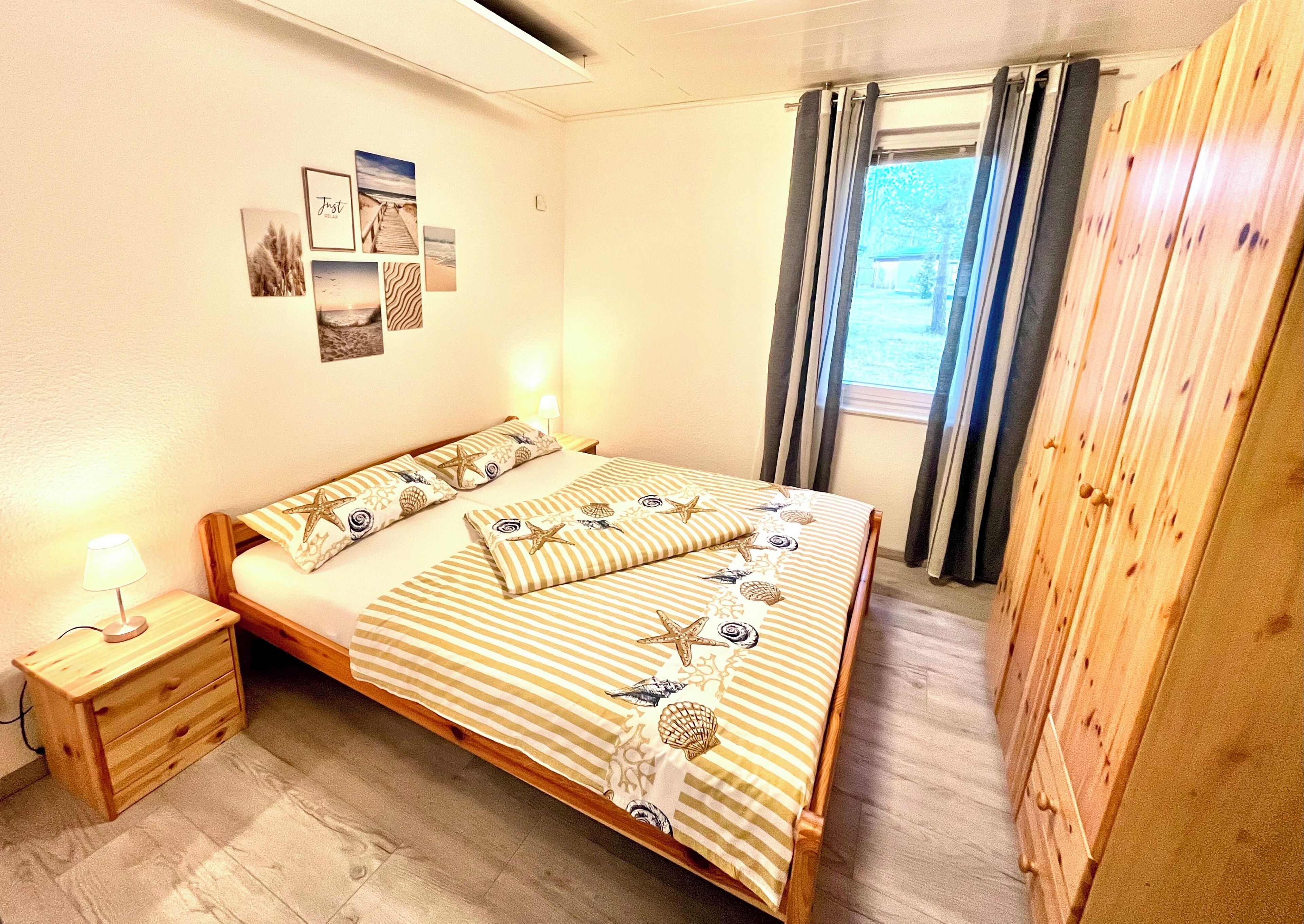 Quarto com cama, mesa de cabeceira, guarda-roupa de madeira e janela com cortinas.