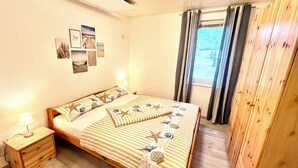 A bedroom with a bed, a nightstand, a wooden wardrobe, and a window with curtains. - Baltic Sea time-out - near Darß - relaxation in the midst of nature (Pruchten)