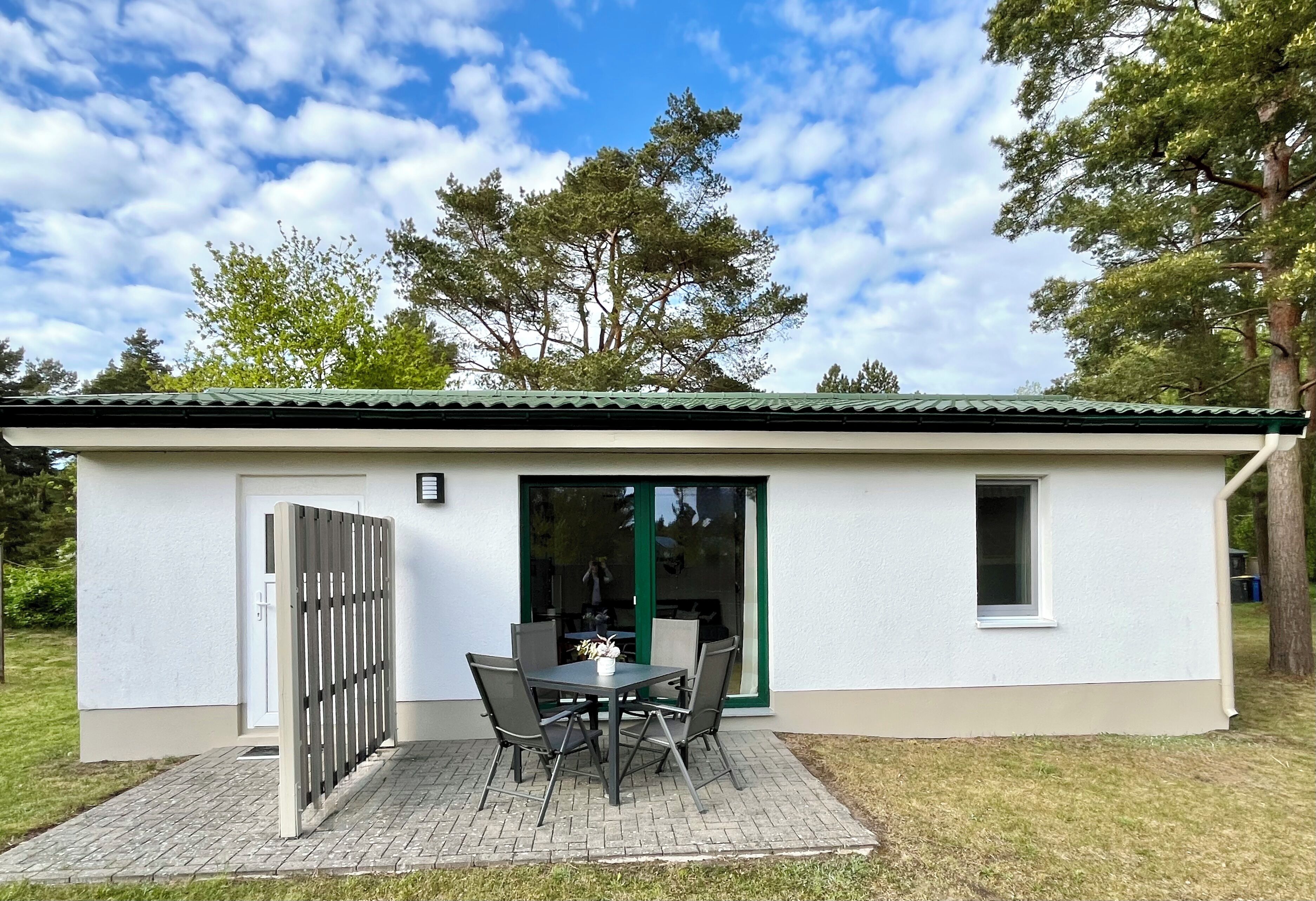 A small, single-story building with a tiled patio, a table with chairs, and a sliding glass door.