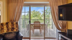 A room with a large sliding glass door leading to an outdoor patio with a table and chairs, a leather sofa, and a television on the right.