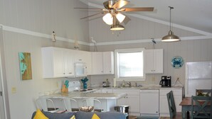 Un espacio habitable compacto con kitchenette, comedor y zona de estar con sofá y sillones.