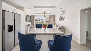 Una cocina moderna con una isla central, dos sillas tapizadas en azul, una mesa de comedor y vistas al exterior.
